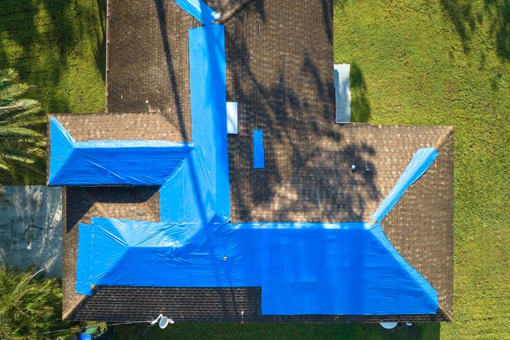 top view leaking house roof covered with protective tarp sheets against rain water-leaks-until-replacement asphalt shingles damage building rooftop